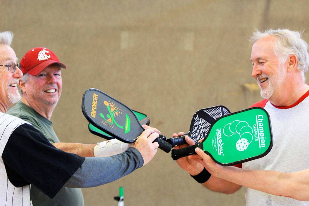 After a game, players Clare Kruse, Dave Meyer, and Barry Haworth (left to right) give the customary high-five slap of their pickle ball racquets. Getting together twice a week to play pickle ball is good for the heart and soul, friendships and fitness, say about 30 participants of the Oak Harbor Senior Center activity. Photo by Patricia Guthrie/Whidbey News-Times