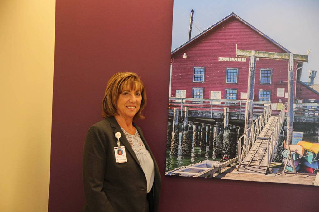 WhidbeyHealth CEO Geri Forbes stands in front of the Whidbey colors used throughout the new addition and next to one of many panoramic photographs taken by local residents and donated by Whidbey Health Foundation. Photo by Patricia Guthrie/Whidbey News Group