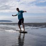 Kyle Jensen / The Record &mdash; Jack&rsquo;d Skimboards owner Auston Reisman glides across a thin layer of water at Double Bluff Beach Friday morning. Reisman is running a two-day summer camp that teaches kids the basics of skimboarding.