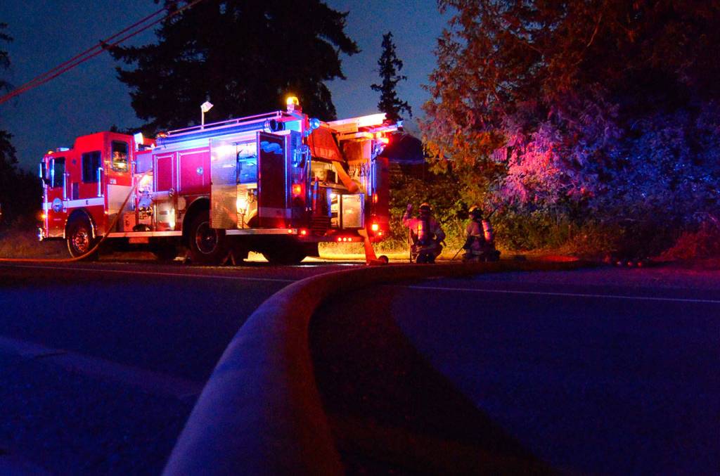 Justin Burnett/The Record &mdash; Two South Whidbey Fire/EMS firefighters wait in reserve at a house fire on Honeymoon Bay Road on Wednesday evening.
