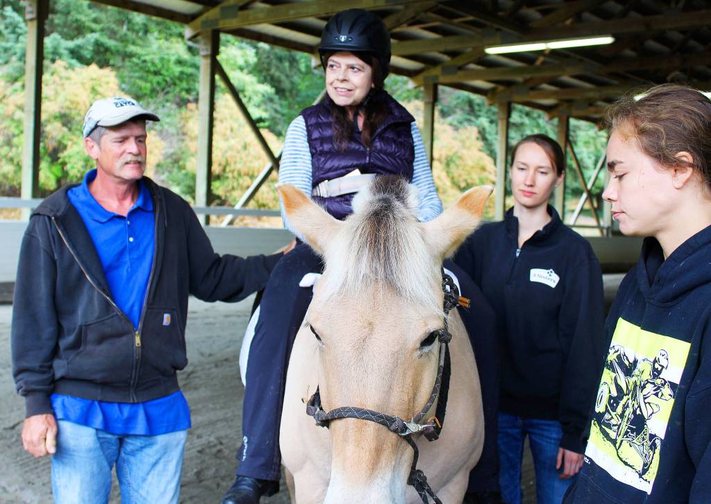 Judy Smith is surrounded by volunteers with Equestrain Crossings while riding in the arena at Whidbey Equestrian Center. Greg Olde and Kellie Holden work as side walkers while Katie Locke (far right) leads the horse. Photo by Patricia Guthrie/Whidbey News-Times