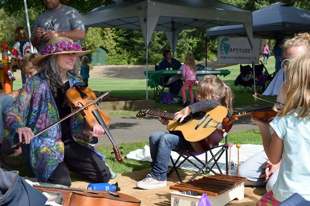 Kyle Jensen / The Record &mdash; More than 30 booths were stationed at Children&rsquo;s Day, including one manned by Island Strings. Instructors like Talia Marcus, left, gave kids quick music lessons.