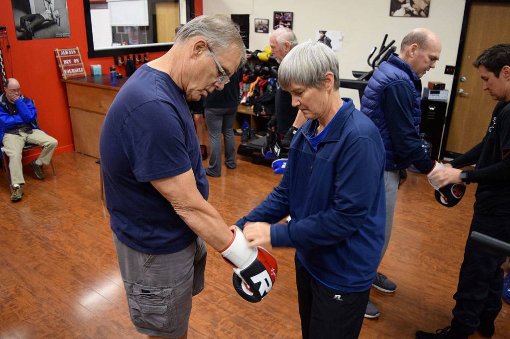Kyle Jensen / The Record  Trainer Sue Taves helps a boxer put on his gloves before the session starts. Taves doesnt have a background in boxing, but was brought into the program as a physical therapist.