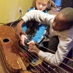 Erick Ngabezaaya (right) shows where to properly place fingers on the Ugandan wooden instrument called an adungo to Shane Astor of Everett.