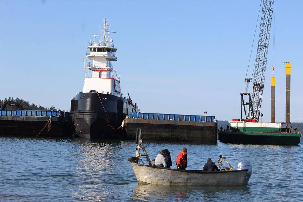 A boat with scuba divers and others heads out to the articulated tug after high tide helped it float into place between two barges.