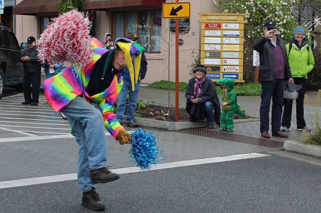 A crocodile sitting on the curb and others along the parade route watch Conducter of Fun Jim Freeman do his thing.