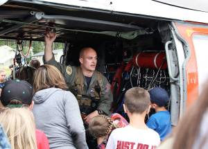 Cody Wall, a member of Search and Rescue from Naval Air Station Whidbey Island, answers questions from a group of children Thursday at Camp Casey Conference Center. The unit landed its helicopter on the camps field to as part of Sea Cadet summer training. The aircraft drew the attention of others present at the camp as well. Photo by Laura Guido/Whidbey News-Times
