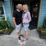 Theron Murphy, of Orem, Utah, kisses his wife, Jody, in front of the John L. Scott Real Estate office in Langley. People stand on the sidewalk on the heart, kiss, then make a hash mark on the chalkboard. The office keeps a tally and posts the monthly and yearly count. (Andy Bronson / The Herald)