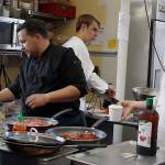 David Phillips, left, leads a crew of young cooks at The South Whidbey Commons Coffeehouse Bookstore in Langley. He created a themed menu this summer for the Island Shakespeare Festival. Caelan Boyd, right, waits to hand Phillips rice while Zakris Pierson slices carrots.(Photo by Patricia Guthrie/Whidbey News Group)