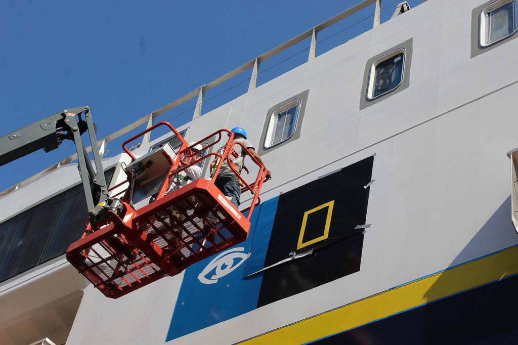 Workers put the finishing touches on the logos of the two companies, Lindblad Expeditions (left) and National Geographic, on the ship named National Geographic Venture.