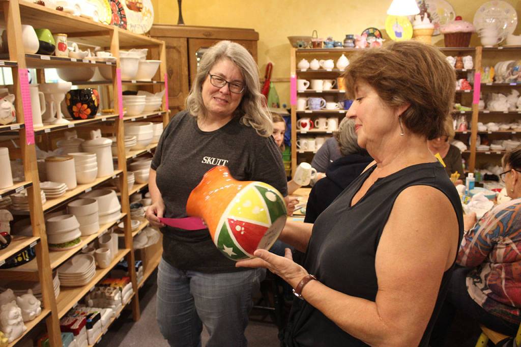 Catherine Vance, right, looks over her finished vase she painted at Whidbey Art Escape with encouragement from owner Tina Beard, left.