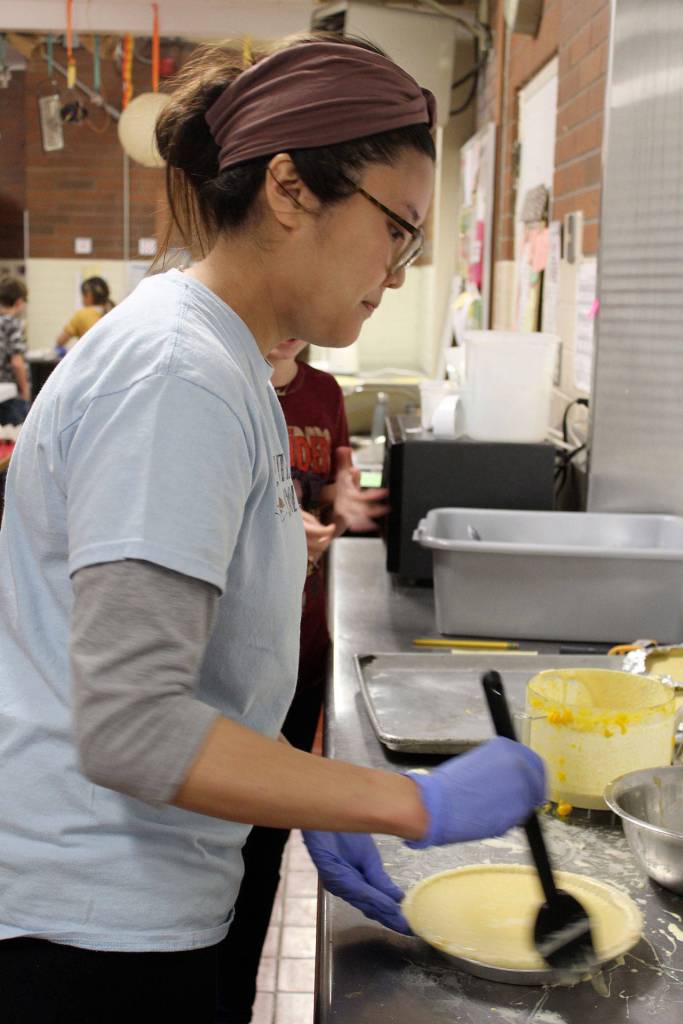 To prevent the pie crust from burning, Tran Hong quickly applies egg wash on the crust before applying aluminum foil strips around the pie.
