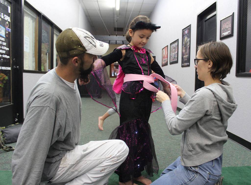 Trinity Rodriguez gets some help with her new pink belt from Jenny Dill as her father, Isaac, looks on.