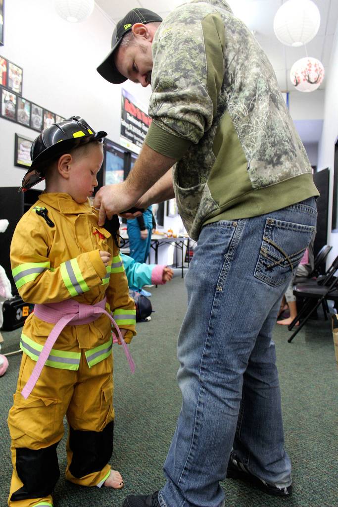 Dillon Rogers, a volunteer firefighter, fixes the firefighting costume of his son, Zachary, at Tuesdays gathering of a taekwondo Tiger class. As a reward for full fundraising participation in the pink belt campaign, the class was treated to a Halloween party by their instructor.