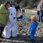 A little tyke wonders why theres a white polar bear at the sandy, sunny beach.