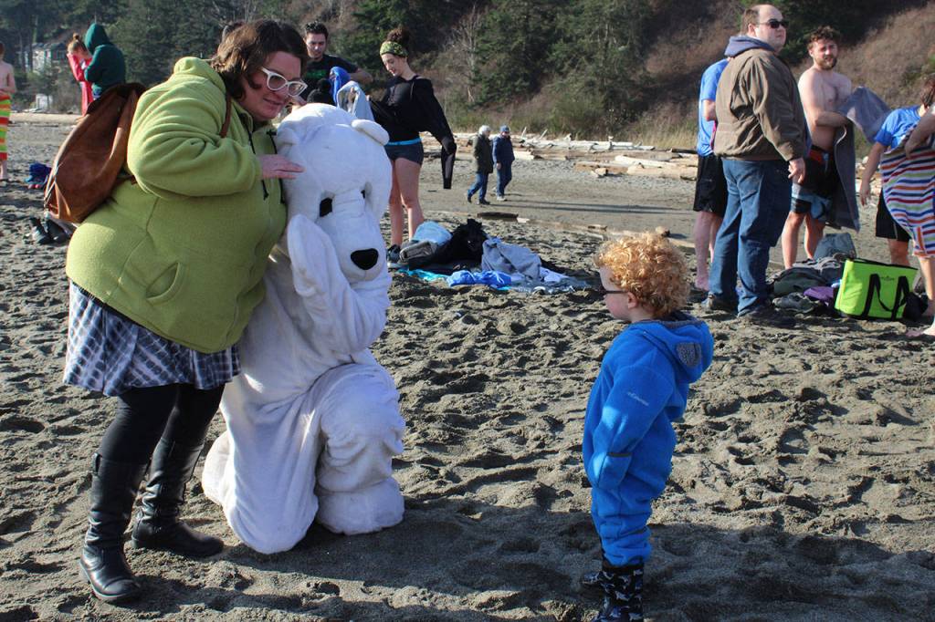 A little tyke wonders why theres a white polar bear at the sandy, sunny beach.