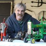 John Norris shows his miniature red Farmall and John Deere green tractors he created out of sewing machines. In the middle is a drag car model made from a pipe wrench. His creations appear at the current Bayview Cash Store recycled art show. (Photo by Patricia Guthrie/Whidbey News Group)