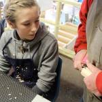 Grace Miller watches closely as Greg Thomas demonstrates the proper carving technique.