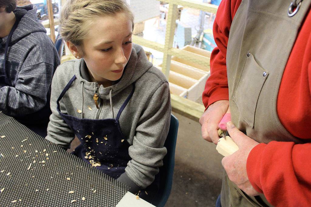Grace Miller watches closely as Greg Thomas demonstrates the proper carving technique.