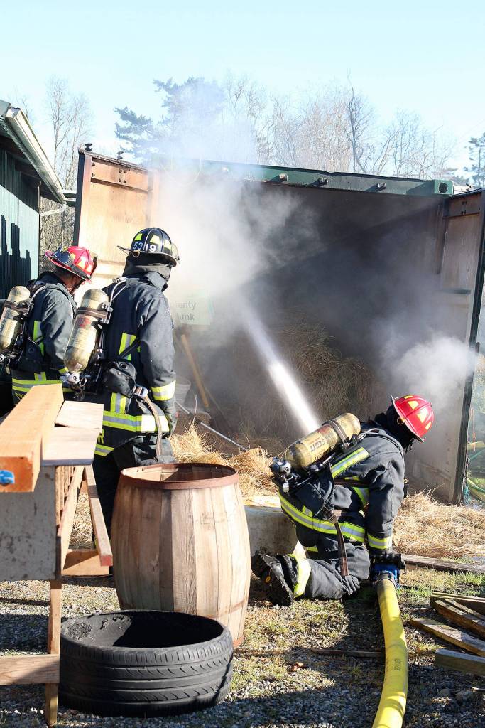 Lt. James Meek, Central Whidbey Island Fire and Rescue, directs a fire hose into a storage container filled with hay. The hay inside caught fire Tuesday when the metal shipping container became too hot from a slow burn outside. Photo by Laura Guido/Whidbey News-Times