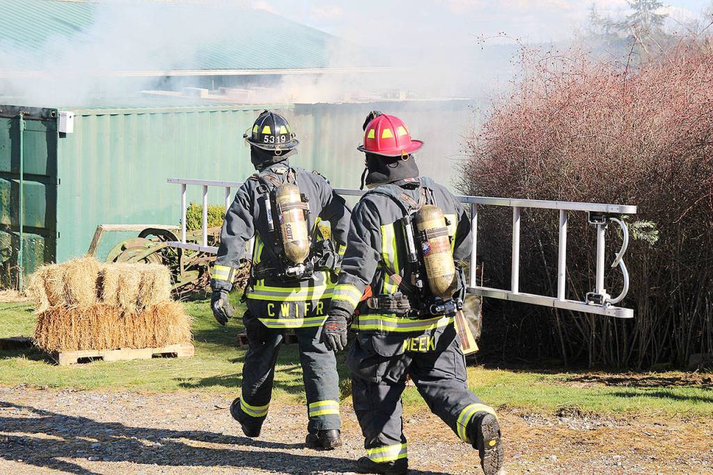 Firefighter/EMT, John Lloyd, front, and Lt. James Meek, with Central Whidbey Island Fire and Rescue carry a ladder to a storage container. The hay inside caught fire Tuesday. Photo by Laura Guido/Whidbey News-Times