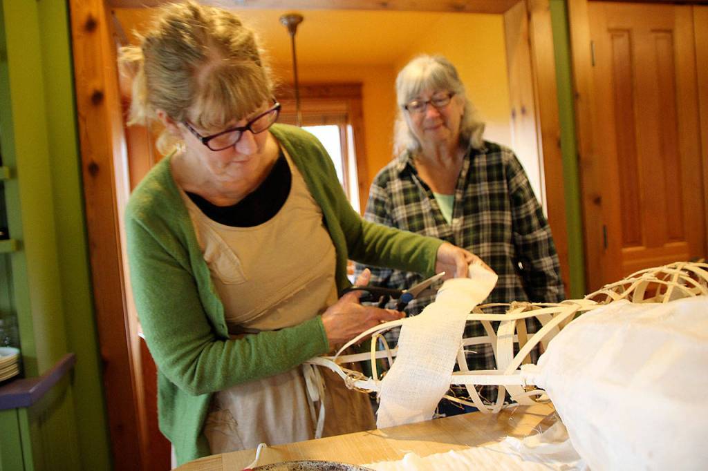 Artist Melissa Koch (front) wraps gauze around the reed skeleton of the five-foot salmon she and Molly Brown are crafting. Their salmon will be featured in the upcoming Welcome the Whales Parade when the city of Langley celebrates the return of traveling gray whales. (Photo by Maria Matson/Whidbey News Group)