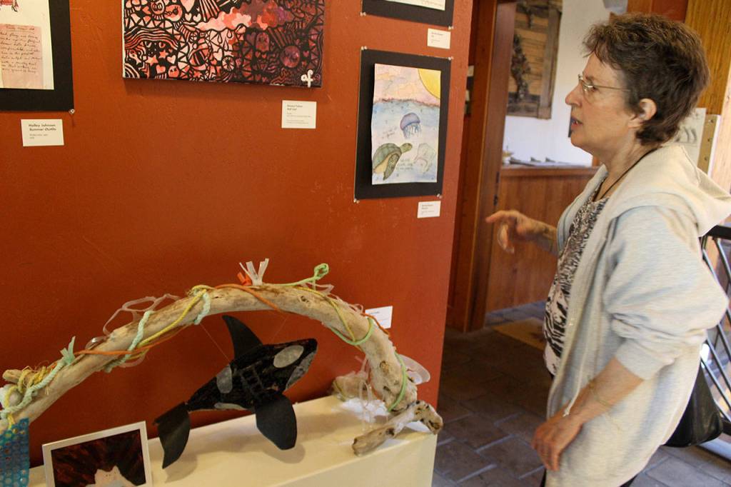 Julie Glover looks over works of art by Whidbey Island high school students, including one titled Detritus displayed on the shelf. Framed in drift wood, the entire three-dimensional piece, including the orca, is made from trash that Emily Fiedler collected from the beach. (Photo by Patricia Guthrie/Whidbey News Group)