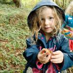 Rainey Stewart, 4, holds a hazelnut shell she found while on a nature walk. Her sister River, 6, looks on. The girls collect discoveries from the forest and use them in their education. Photo by Kira Erickson/Whidbey News-Times