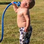 Ian Lambert, 13 months old, plays with a hose to stay cool.