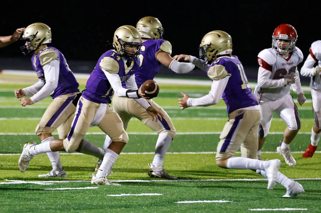 Oak Harbor High School senior Kaito White, left, hands off the ball to sophomore Brody Snyder during the homecoming game Sept. 17 against Stanwood High School. The Wildcats lost to the Spartans 34-14. (Photo by John Fisken)
