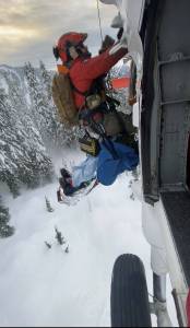 A Navy Search and Rescue Medical Technician, HM1 Thomas Molnar helps hoist an injured man into Naval Air Station Whidbey Island’s SAR helicopter in the Cascade Mountains during a rescue mission on January 29, 2021. Official Navy photo by AWS1 Ricardo Rosado.