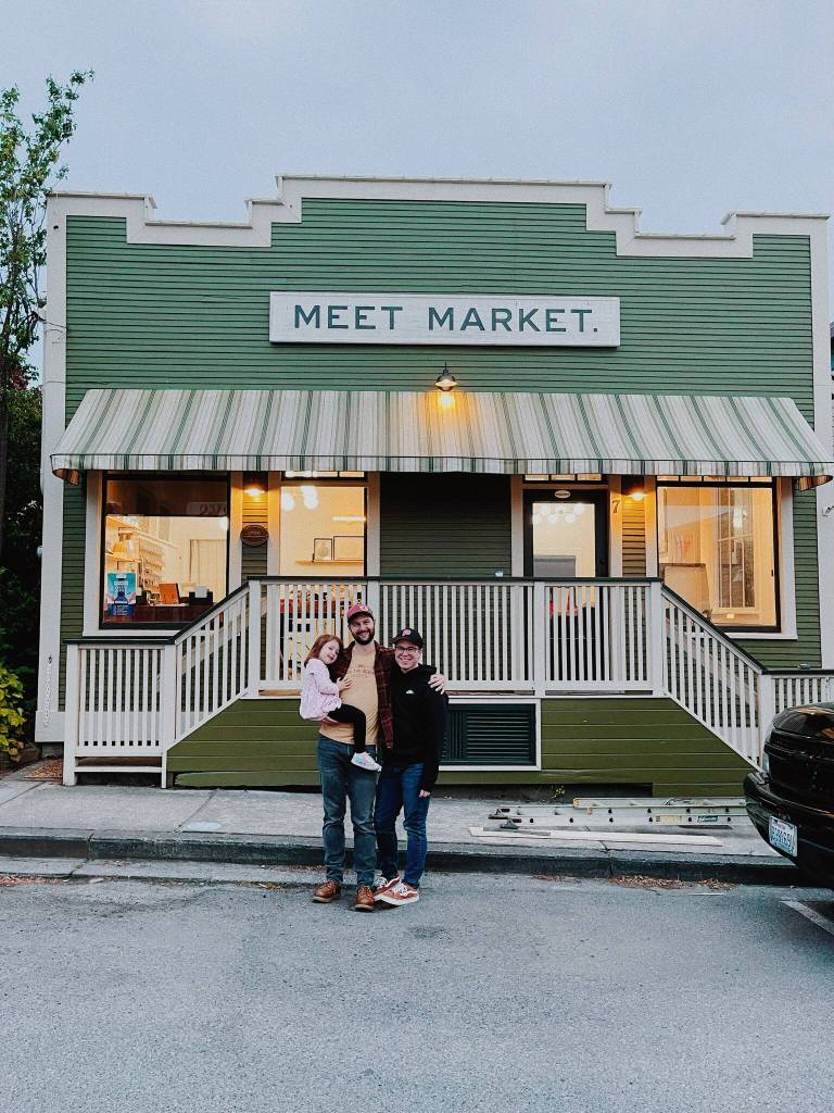 Andrew Ziehl, center, and Cade Roach stand in front of their new business, Meet Market, with their daughter, Eliot. (Photo provided)