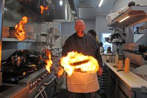 Chef Gordon Stewart adds a fiery flare to a dish in the kitchen at Gordons Fusion. (Photo by Karina Andrew/Whidbey News-Times)