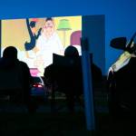 People sit in lawn chairs and watch a Looney Tunes short at the Blue Fox Drive-In Theater in Oak Harbor. (Ryan Berry / The Herald)