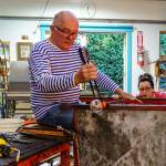 Photo by David Welton
John de Wit shapes a piece of glass while Catherine Marshall blows the glass.