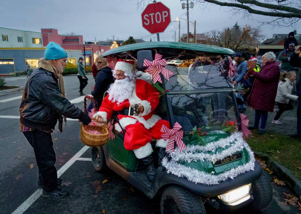 Photo by David Welton
Riding in a golf cart, Santa receives some assistance from merchant Fred Lundahl, who owns Music for the Eyes.