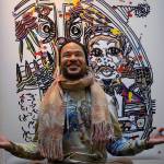 Photo by David Welton
Dressed in brightly tie-dyed clothing he made himself, Ian Joseph Jackson strikes a meditative pose in front of his artwork that includes Martin Luther King Jr. at the podium.