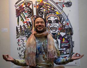Photo by David Welton
Dressed in brightly tie-dyed clothing he made himself, Ian Joseph Jackson strikes a meditative pose in front of his artwork that includes Martin Luther King Jr. at the podium.