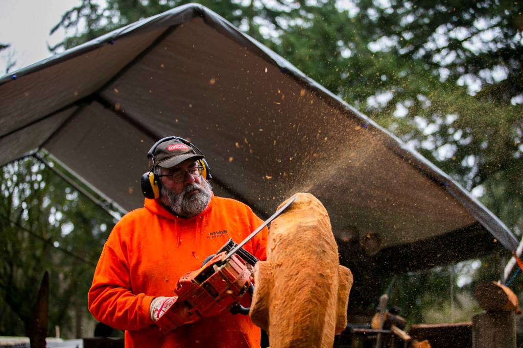 Flakes of wood and sawdust spray in different directions while Steve Backus works on the details of a moon carving. (Olivia Vanni / The Herald)