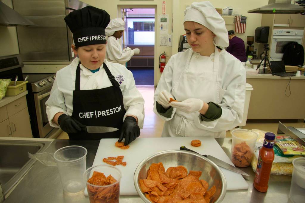 Preston Huessman (left), with the help of high schooler Sam Ross McMahon, prepared a pizza salad with pepperoni and lettuce. (Photo by Rachel Rosen/Whidbey News-Times)