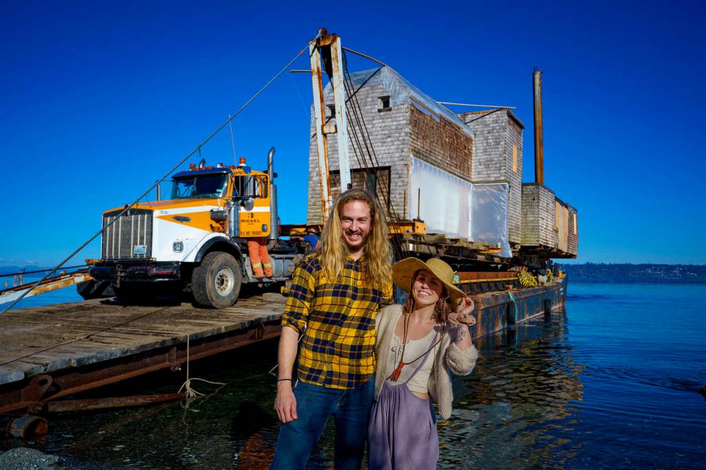 Tevon Dubois and Chanel Jost pose in front of their house as it is loaded onto a truck at a Possession Point dock. (Photo by David Welton)