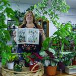 Geneva Blackmer holds some prints surrounded by a collection of plants. (Photo by Luisa Loi)