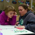 Third grader Irene Doleshel works on a poster about pollinator habitats with the help of mother Ali. (Photo by David Welton)