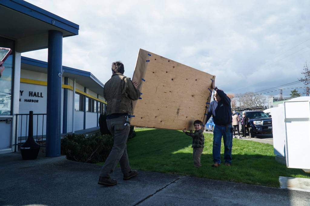 Artist Nick Mann (left), his son George Mann (middle) and faculties worker Tom Wade (right) bring a panel of Song of the Salish Sea into City Hall. (Photo by Sam Fletcher)