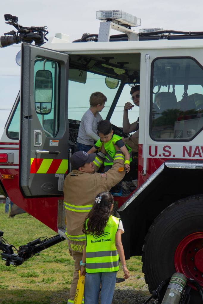 Photo by Caitlyn Anderson
Navy firefighter Dakota Montoya lifts Oliver Brower out of an E-ONE ARFF at the Touch-a-Truck event.