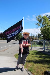 Photo by Luisa Loi
Pam Fick holds a flag and wears a Handmaids Tale shirt. The Handmaids Tale is the story about a society were women are completely subservient to men and have no reproductive freedoms, which Fick believes could become a reality.