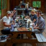 Organic Farm School students enjoy a meal of wood-fired pizza after a long day of harvesting chickens. (Photo by David Welton)