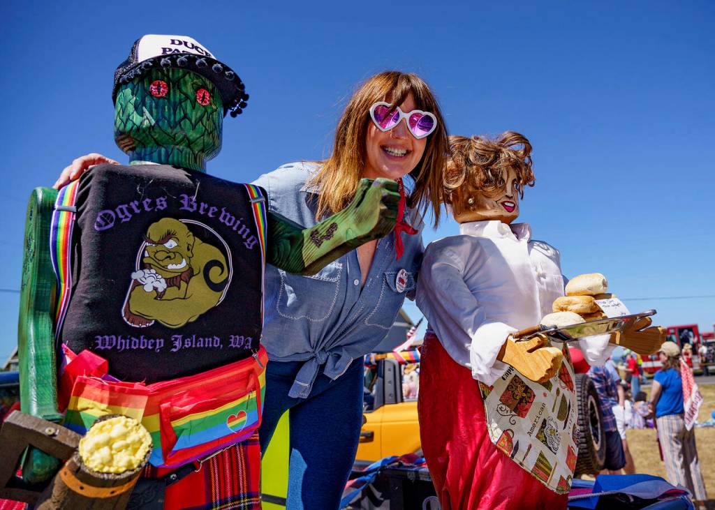 Photo by David Welton Emily Spitzer, president of Clinton Chamber of Commerce, is with the wooden statues carved by Kelly from Madrone.