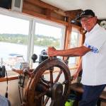 Dennis Redmon poses behind the steering wheel. The boats two steering wheels are the only part of the original boat that are left above the engine room area. Originally the wheels were wrapped with ropes that went down through pulleys and moved the rudder. The Redmons kept the appearence of the original wheels which now control hydraulic steering pumps. (Photo by Luisa Loi)