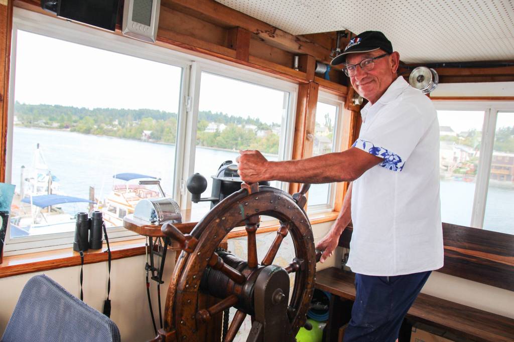 Dennis Redmon poses behind the steering wheel. The boats two steering wheels are the only part of the original boat that are left above the engine room area. Originally the wheels were wrapped with ropes that went down through pulleys and moved the rudder. The Redmons kept the appearence of the original wheels which now control hydraulic steering pumps. (Photo by Luisa Loi)